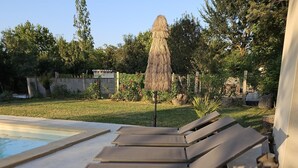 Un espace aménagé au bord de la piscine, avec des chaises longues et un parasol en chaume.