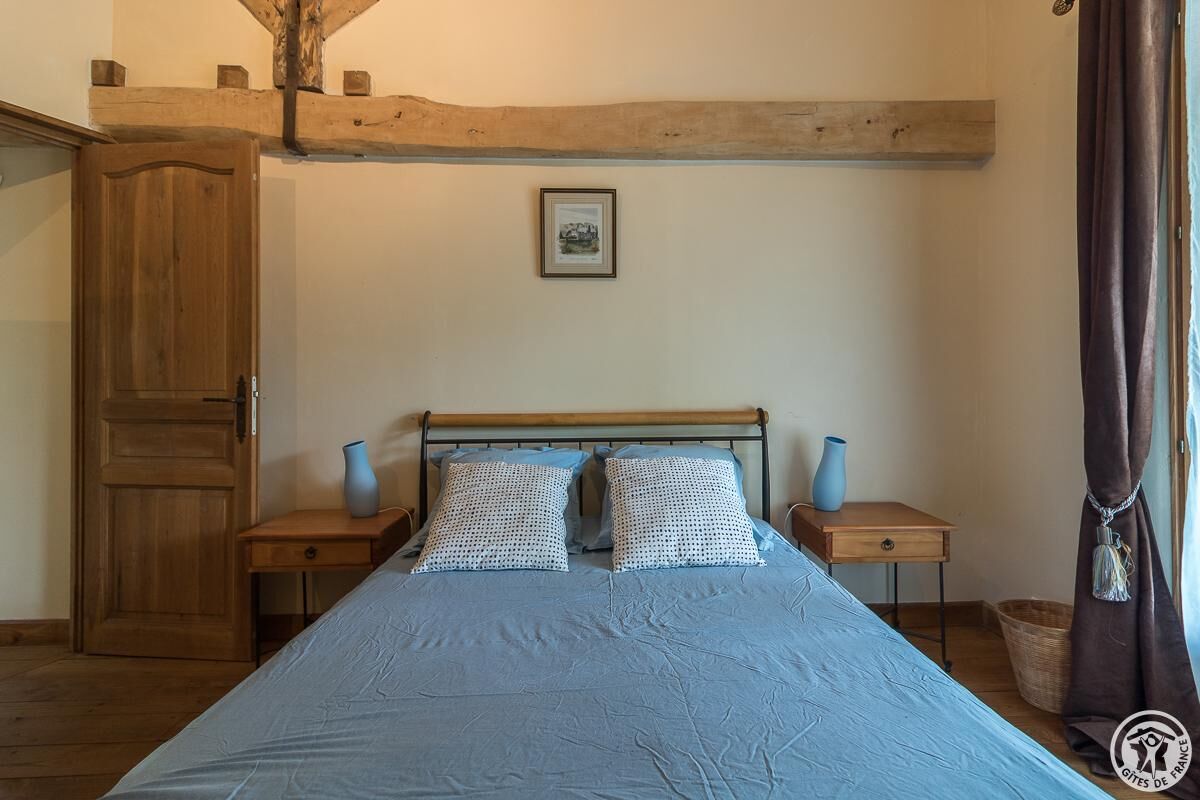 A bedroom with a wooden bed frame, two matching pillows, a framed picture on the wall, and a wooden door.