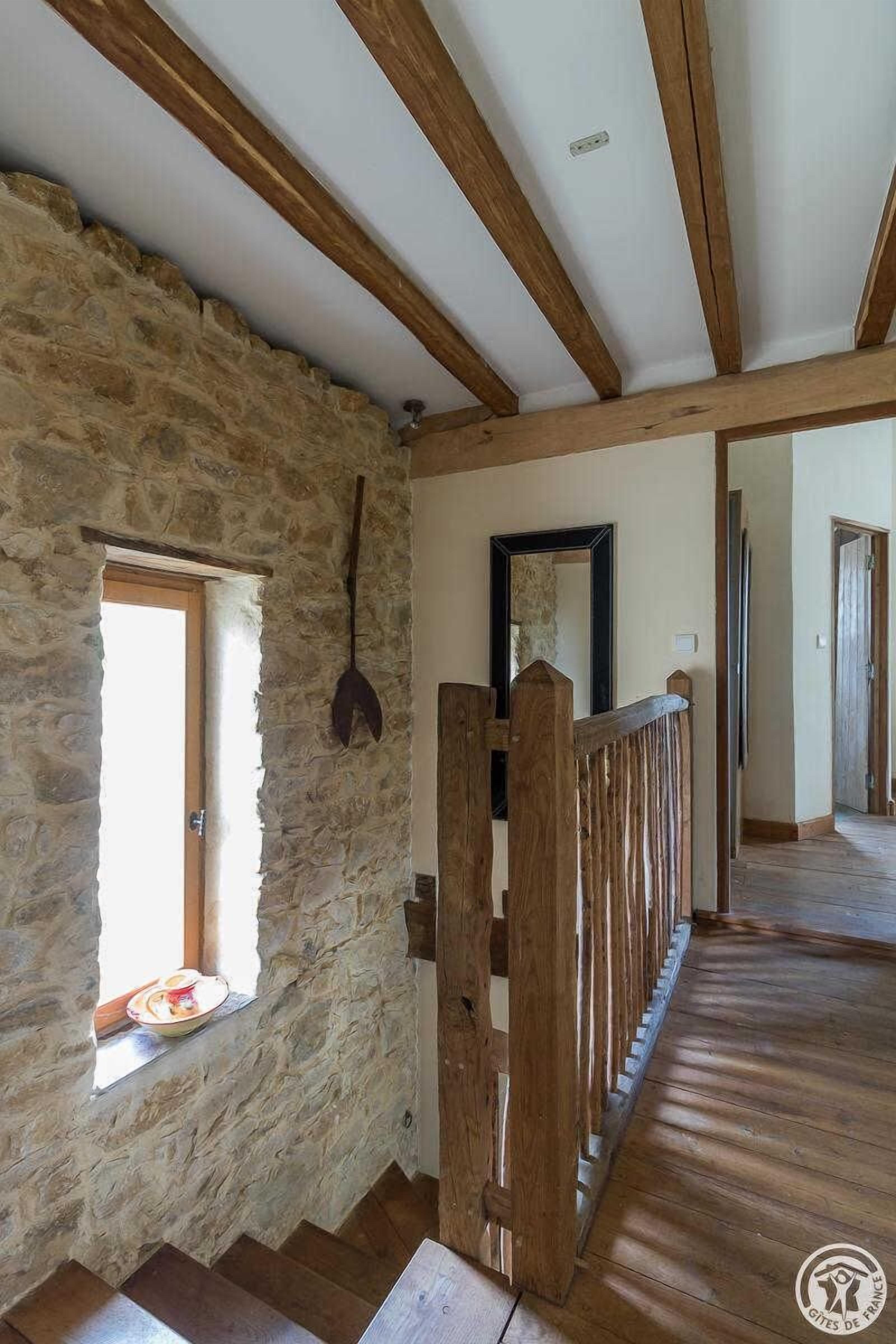 A rustic interior with stone walls, wooden beams, a wooden gate, and a window with a plate.