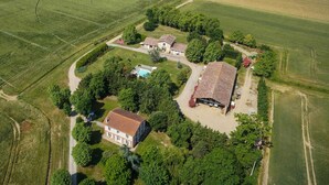 An aerial view of a rural property with multiple buildings, including a large barn and residential houses, surrounded by fields and trees.