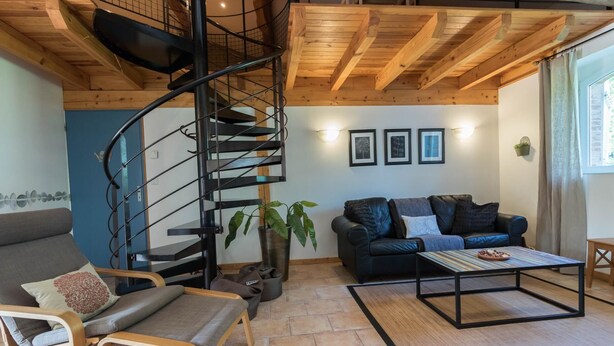 A modern living room with a spiral staircase, a black leather sofa, a wooden coffee table, and a potted plant.