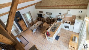 A kitchen with a dining area, wooden beams, a brick wall, and a window.