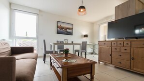 A modern living room with a sofa, a wooden coffee table, a dining table with chairs, a TV, and a cabinet.