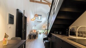Una cocina moderna con encimera negra, zona de comedor con mesa y sillas, y escalera que sube a un nivel superior.