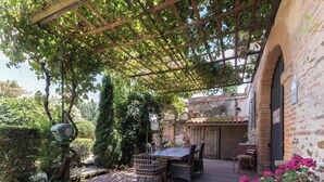 Un patio exterior con una pérgola, una mesa, sillas y un muro de ladrillo.