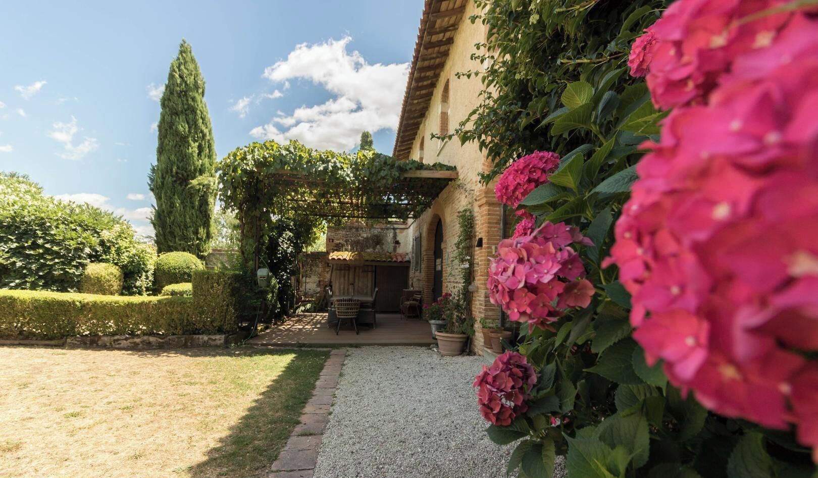 Ein Garten mit einer Pergola, einem Kiesweg und Kübelpflanzen.