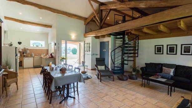 Amplia sala de estar con mesa de comedor, una escalera y una cocina al fondo.