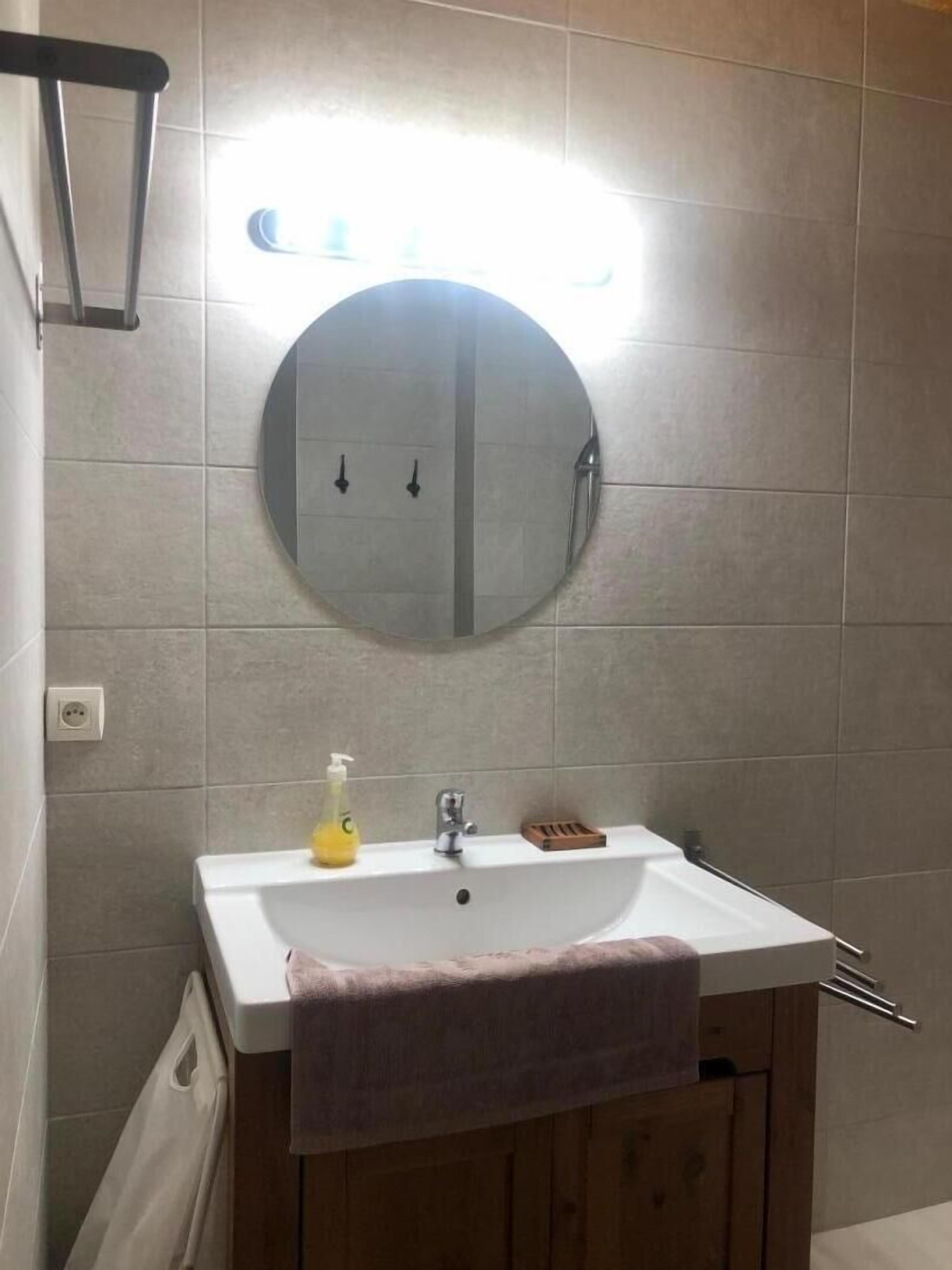 Un baño con un espejo redondo, un lavabo blanco, un dispensador de jabón y una toalla colgada en la pared.