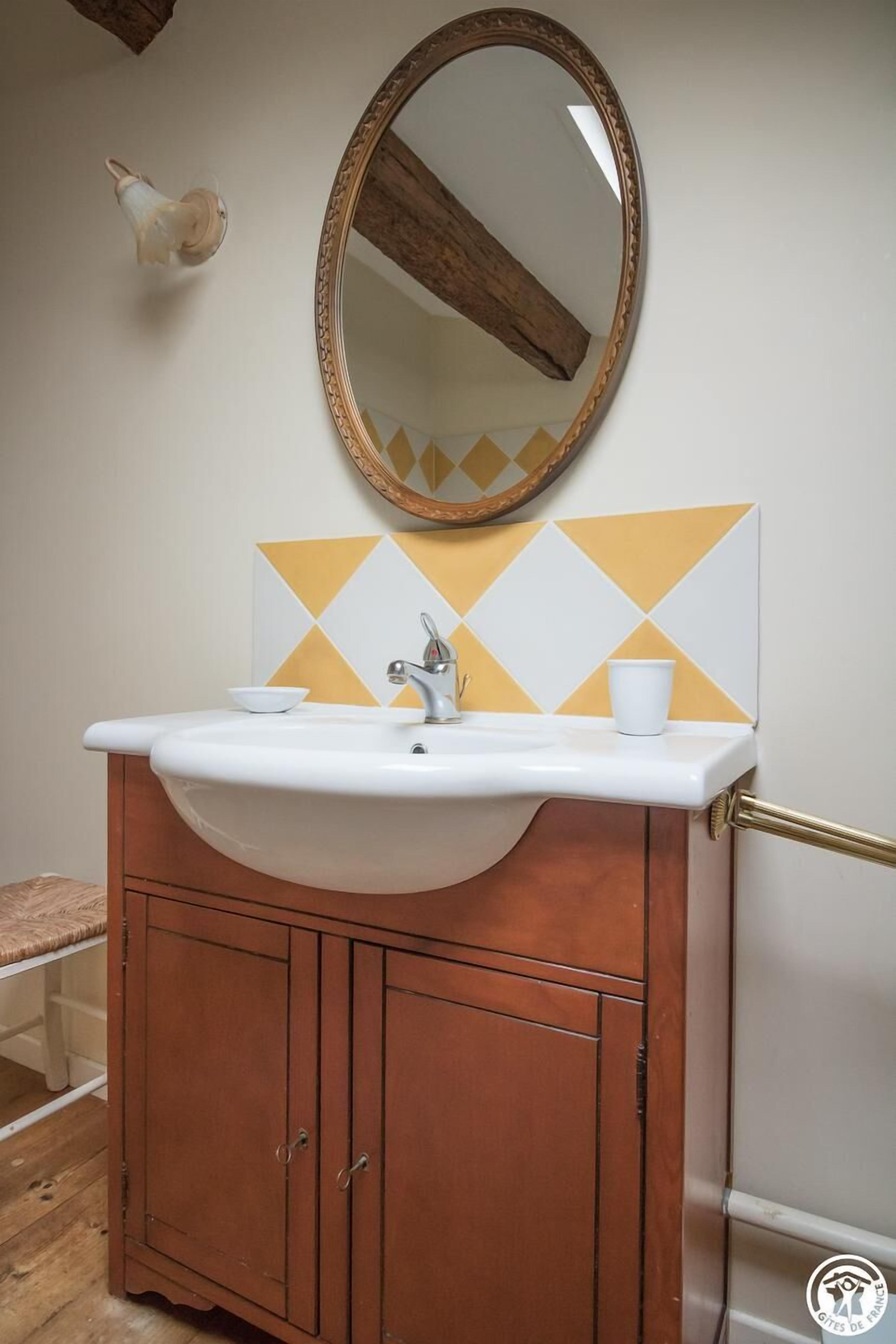 A bathroom with a white sink, wooden cabinet, and a mirror with a decorative frame.