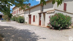 A traditional building with a gravel driveway, wooden shutters, and a well-maintained garden with flowering plants. - Domaine de Blanconne (Léguevin)