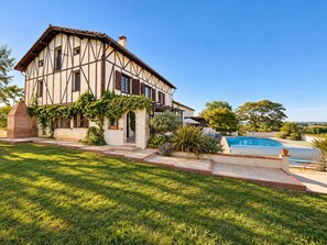 Une maison à deux étages avec une piscine, entourée d’une pelouse et d’un jardin bien entretenus.