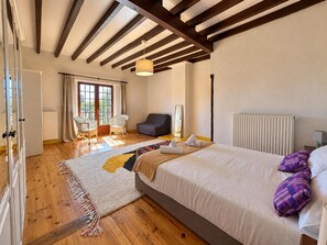 Une chambre à coucher avec un grand lit, un plancher en bois, une fenêtre avec des rideaux, une chaise et un radiateur.