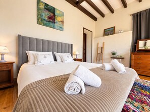 Une chambre d’hôtel avec un grand lit, une commode en bois, un tableau au mur et une fenêtre avec des rideaux.