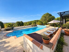 Une piscine sur le toit offrant une vue dégagée sur le paysage environnant, une pergola avec un auvent et des chaises longues.