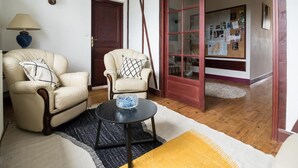 Una sala de estar con dos sillones color crema, una mesa de centro negra con un cuenco de vidrio, una lámpara y suelo de madera.