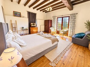 Une chambre à coucher avec un grand lit, un plancher en bois, une commode, une chaise et une vue sur l’extérieur par une fenêtre.
