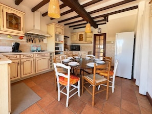 Une cuisine avec des meubles de rangement en bois, une table à manger pour quatre personnes et un luminaire suspendu.