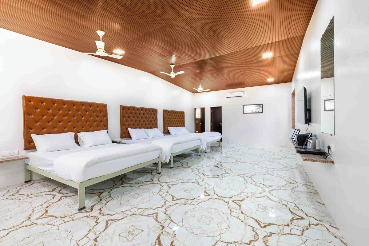 Quarto de hotel com três camas, teto de madeira e piso estampado.