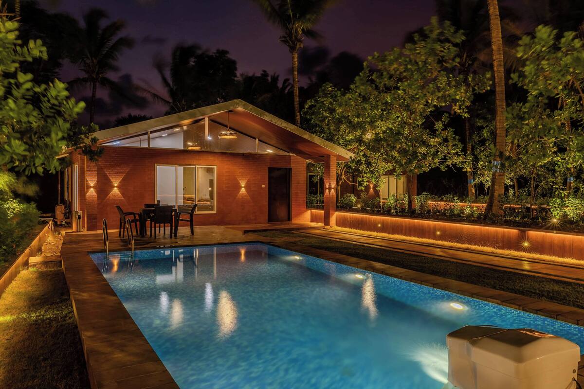 Uma casa moderna com piscina, cercada por palmeiras e áreas externas bem iluminadas.