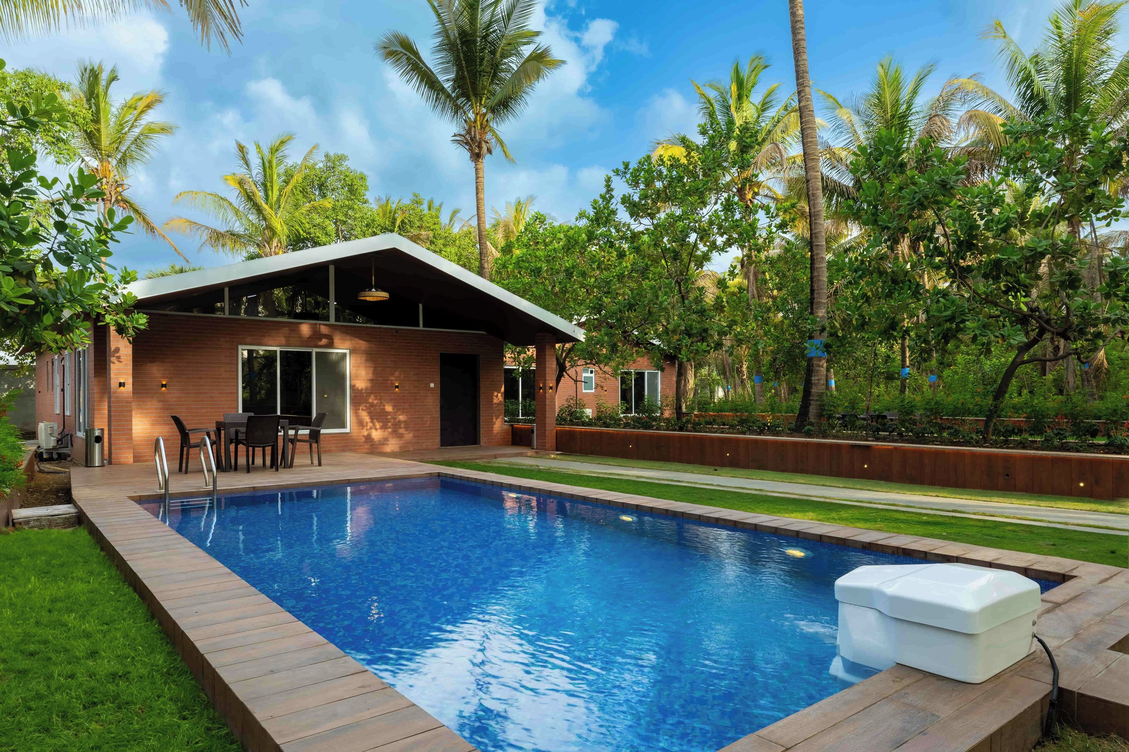 A modern house with a swimming pool, surrounded by lush greenery and palm trees.
