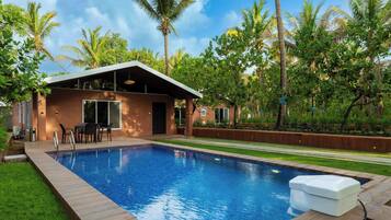 A modern house with a swimming pool, surrounded by lush greenery and palm trees.