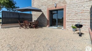 Une terrasse extérieure avec une table et des chaises, un barbecue et un bâtiment à la façade en briques.