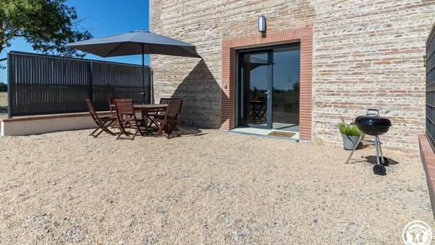 Une terrasse extérieure avec une table et des chaises, un barbecue et un bâtiment à la façade en briques.