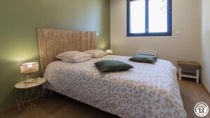 Une chambre à coucher avec un lit, une lampe de chevet, une fenêtre et un petit banc.