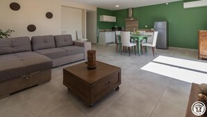 Un salon moderne avec un canapé gris, une table basse en bois et un coin repas comprenant une table verte et des chaises blanches.
