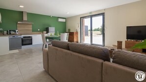 Un salon moderne comprenant un canapé, un téléviseur et un coin cuisine avec une table à manger.