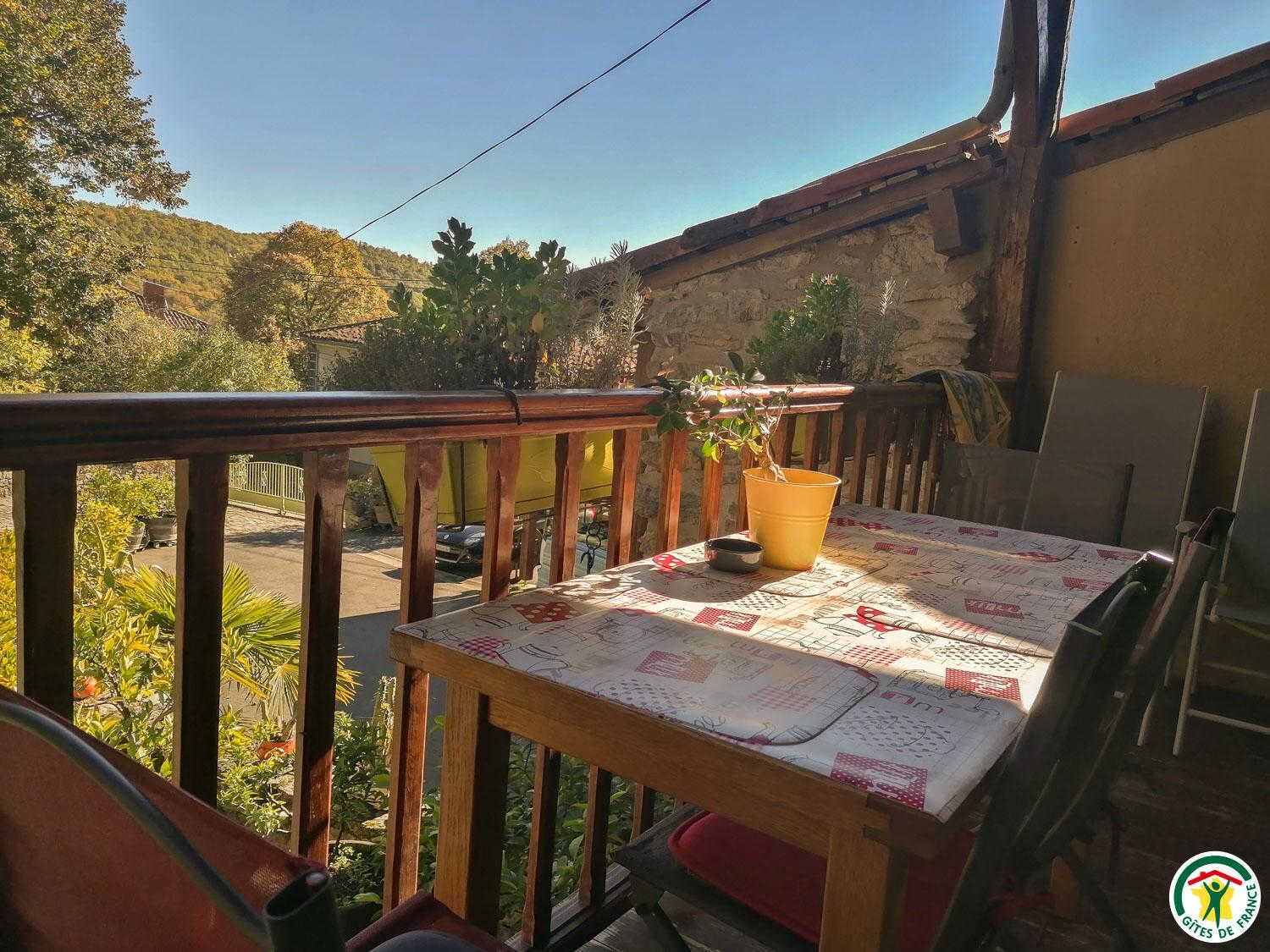 Un balcon avec une table et des chaises, un pot de fleurs et une vue sur une rue et des arbres.