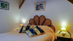 A bedroom with a wooden headboard, a bed with a white duvet and patterned pillows, a nightstand with a lamp, and two framed pictures on the wall. - La Grande Ourse - Montespan (Montespan)