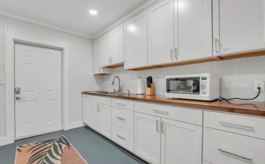 A modern kitchen with white cabinets, a wooden countertop, and a microwave.