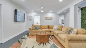 A modern living room with a sectional sofa, a woven coffee table, and a flat-screen TV mounted on the wall. - 3-Bed, 1-Bath Comfort & Style
 (Tybee Island)