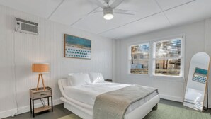 A bedroom with a bed, a standing lamp, a painting, a window with blinds, and a ceiling fan. - 3-Bed, 1-Bath Comfort & Style
 (Tybee Island)