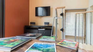 A room with a wooden table displaying travel books, a television mounted on the wall, and a window with blinds. - Las Brancas - Cessales (Cessales)