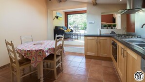 A spacious kitchen with wooden cabinets, a dining area with a table and chairs, and a view of the outdoors. - Las Brancas - Cessales (Cessales)