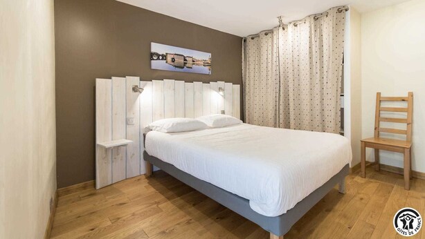 A bedroom with a bed, a nightstand, a chair, a wall-mounted lamp, and a curtain. - Las Brancas - Cessales (Cessales)
