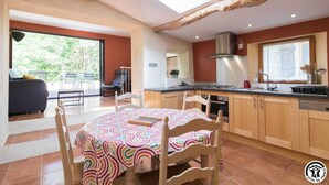 A spacious kitchen with wooden cabinets, a large window, and a dining area with a colorful tablecloth. - Las Brancas - Cessales (Cessales)
