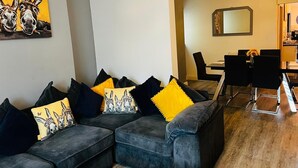 Ein modernes Wohnzimmer mit einem grauen Ecksofa, schwarzen und gelben Kissen und einem Gemälde von Eseln an der Wand.