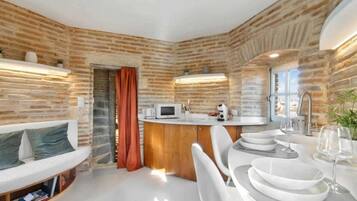 Une cuisine compacte avec un mur en briques, un plan de travail blanc et un coin repas avec des chaises et des assiettes blanches.