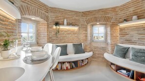 A room with exposed brick walls, a white sofa, a dining table with chairs, and a bookshelf integrated into the seating area.