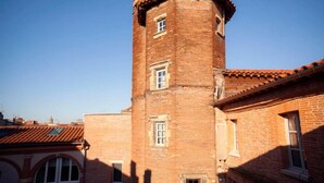 A brick tower with a rounded top and windows, part of a building with a tiled roof.