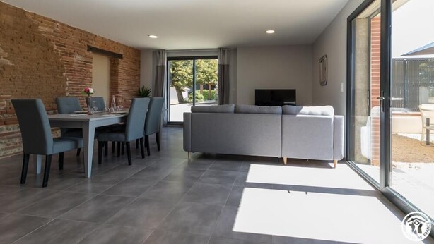 A modern living room with a grey sofa, dining table with chairs, and a TV. - Domaine le Caprougeat - Chic countryside (Daux)