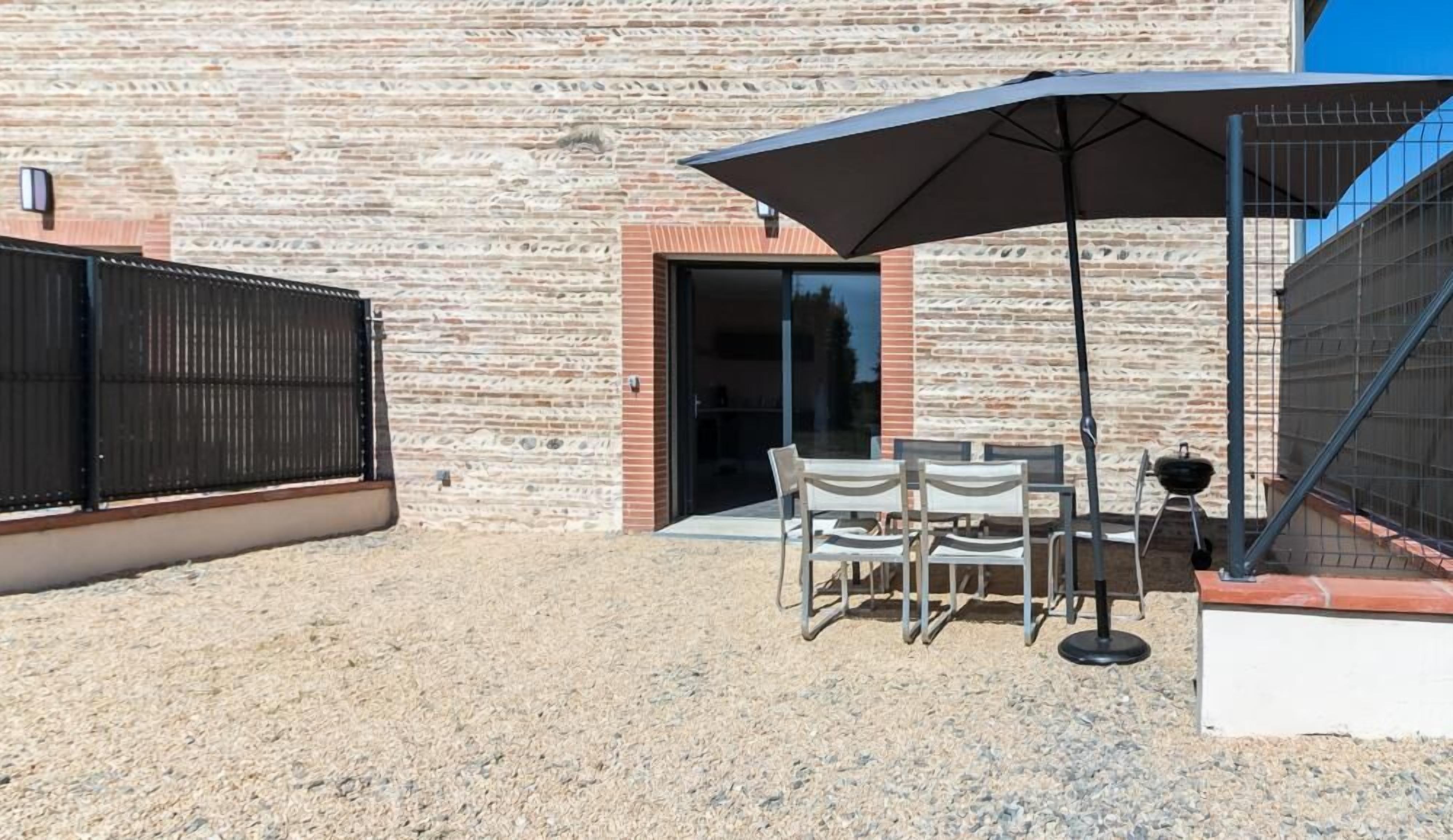 Eine Terrasse mit Tisch und Stühlen, einem großen Sonnenschirm und einem Grill.