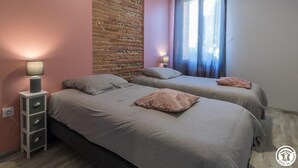 A bedroom with two beds, a brick wall, and a window with curtains. - Domaine le Caprougeat - Chic countryside (Daux)