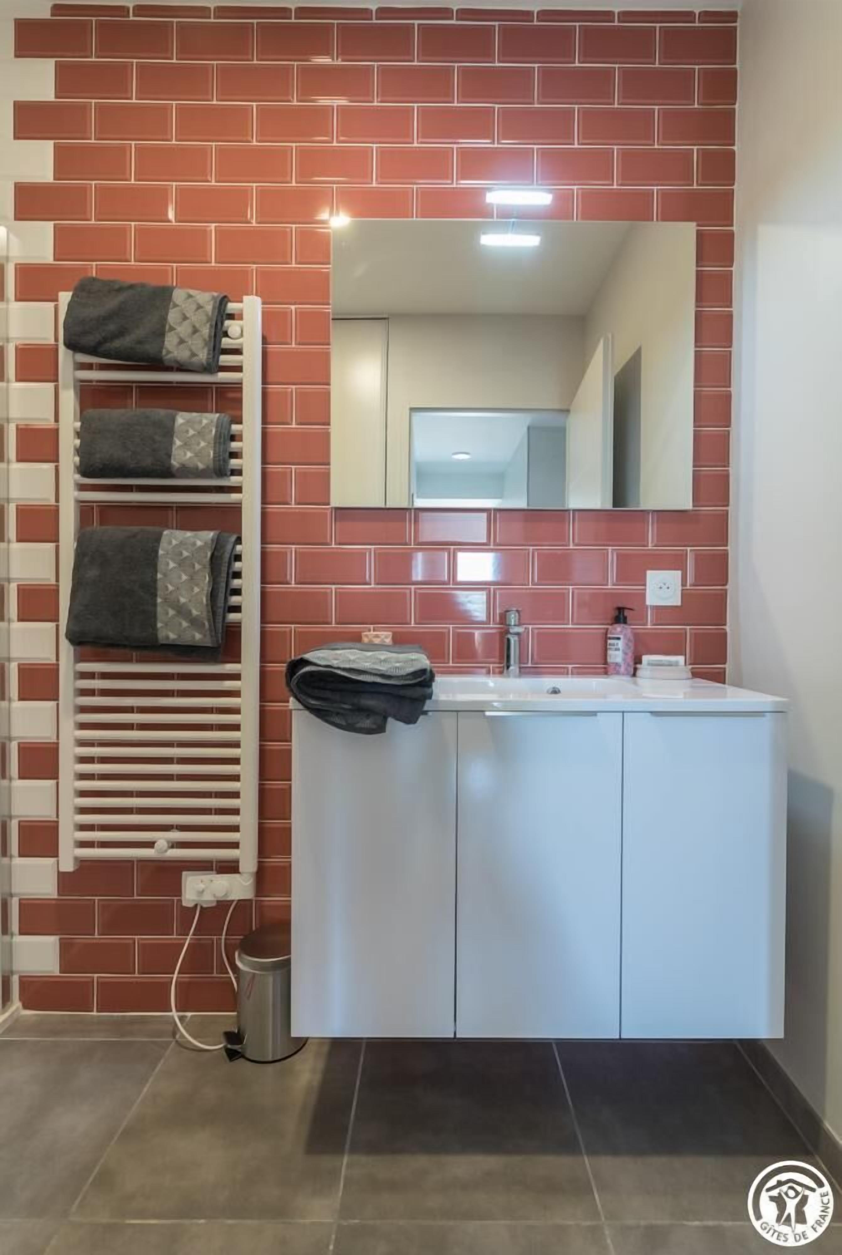 A bathroom with a red-tiled wall, a white sink, and a towel rack with folded towels.