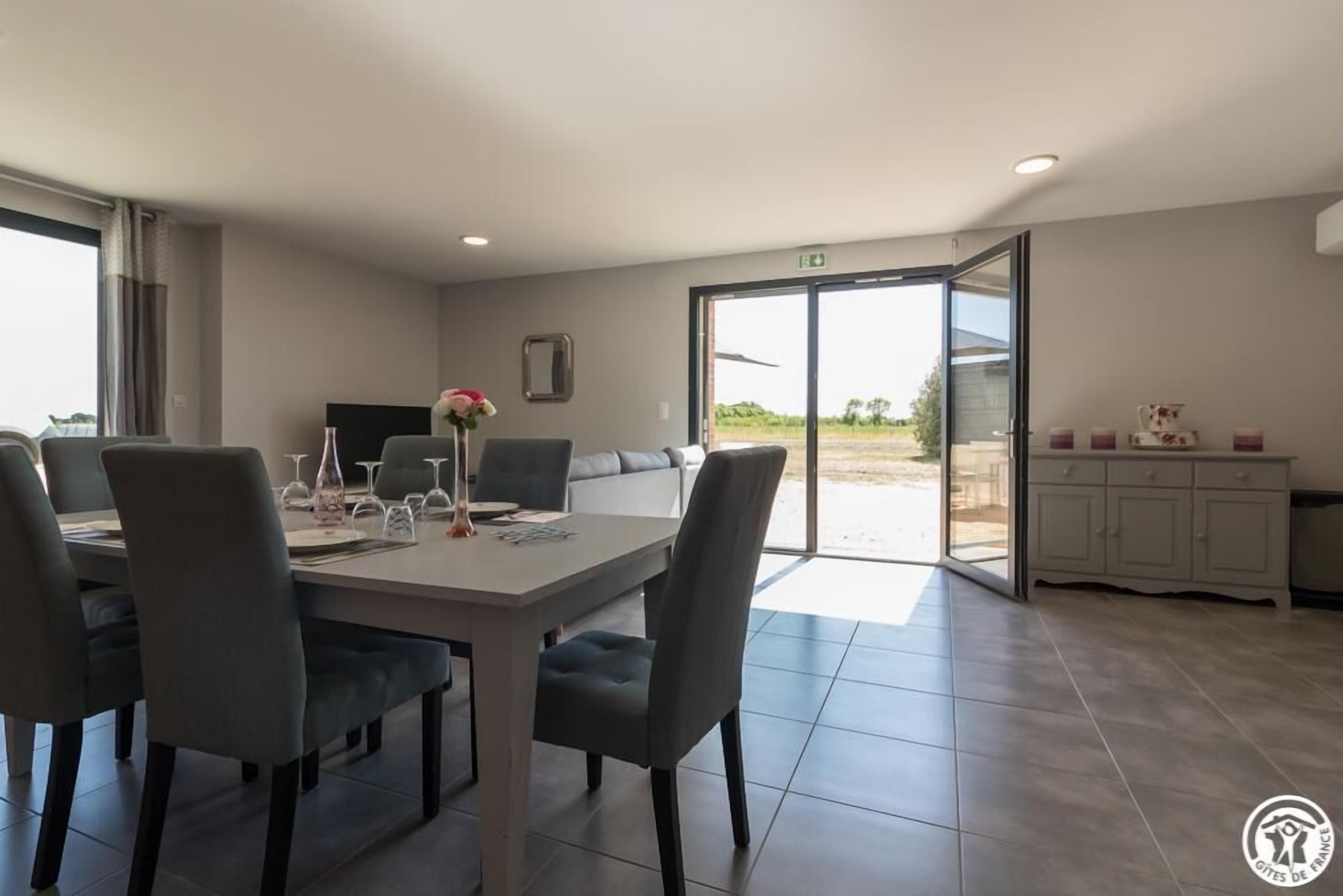 A modern dining area with a table set for four, a sofa, and a kitchen area visible through an open door.