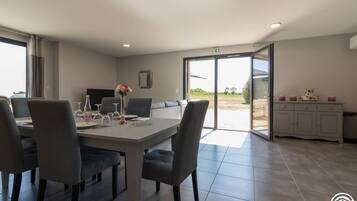A modern dining area with a table set for four, a sofa, and a kitchen area visible through an open door.