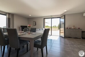 Un espace repas moderne avec une table dressée pour quatre personnes, un canapé et un coin cuisine visible à travers une porte ouverte.